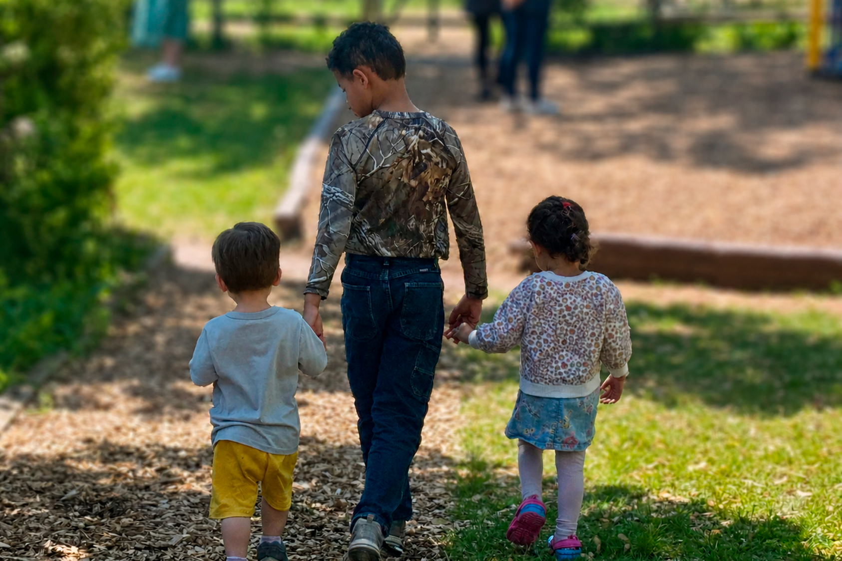 Elementary student walking toddlers through nature path