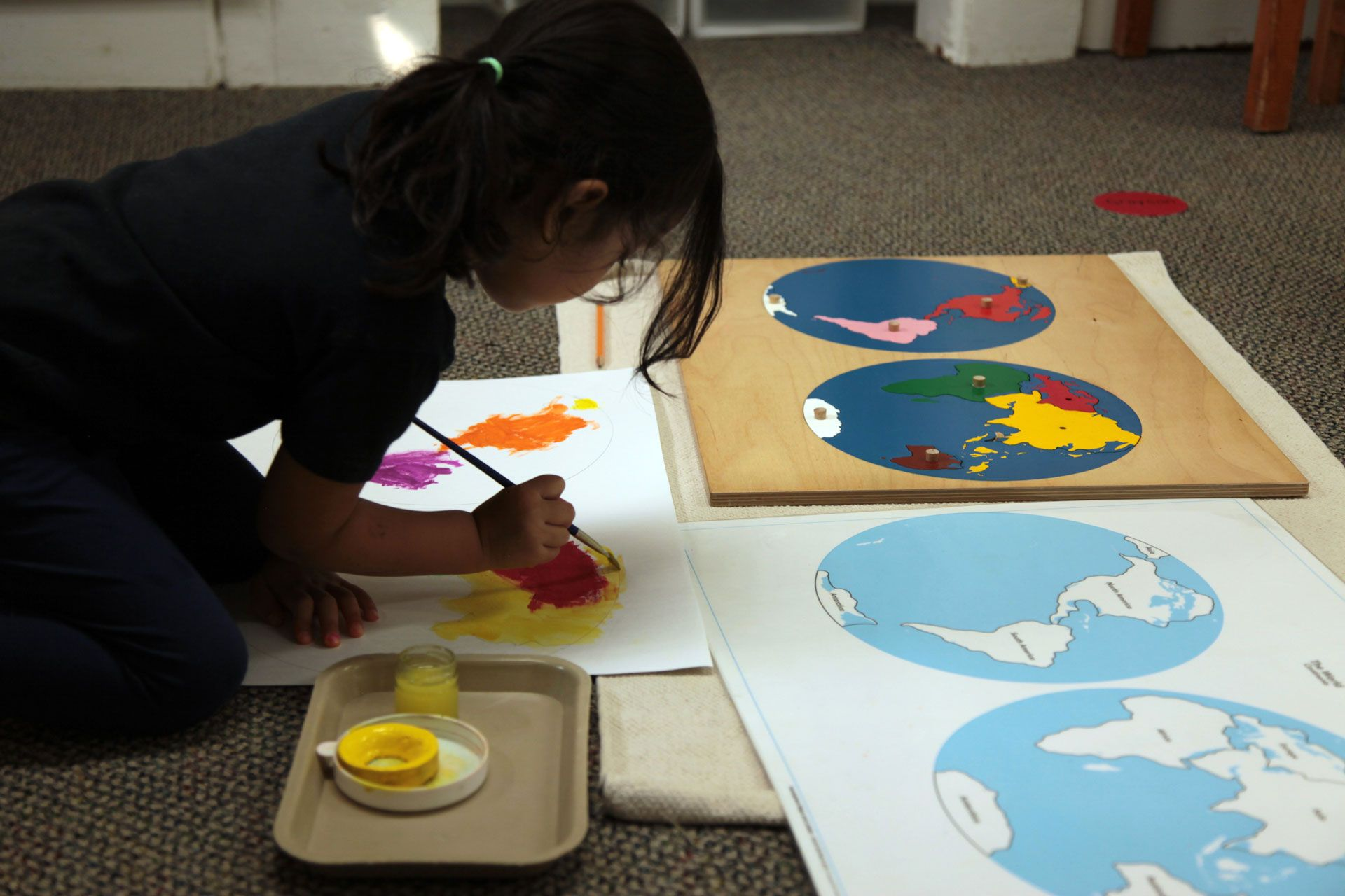 Montessori child painting the continents after using the world puzzle map