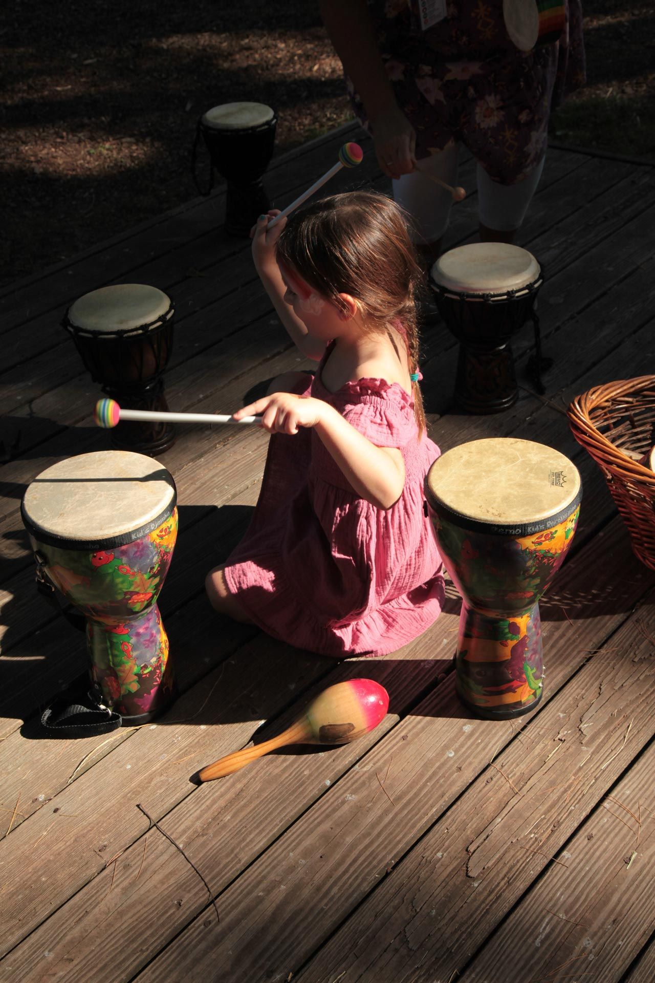 Montessori primary child kneeling on a wooden deck playing a djembe drum