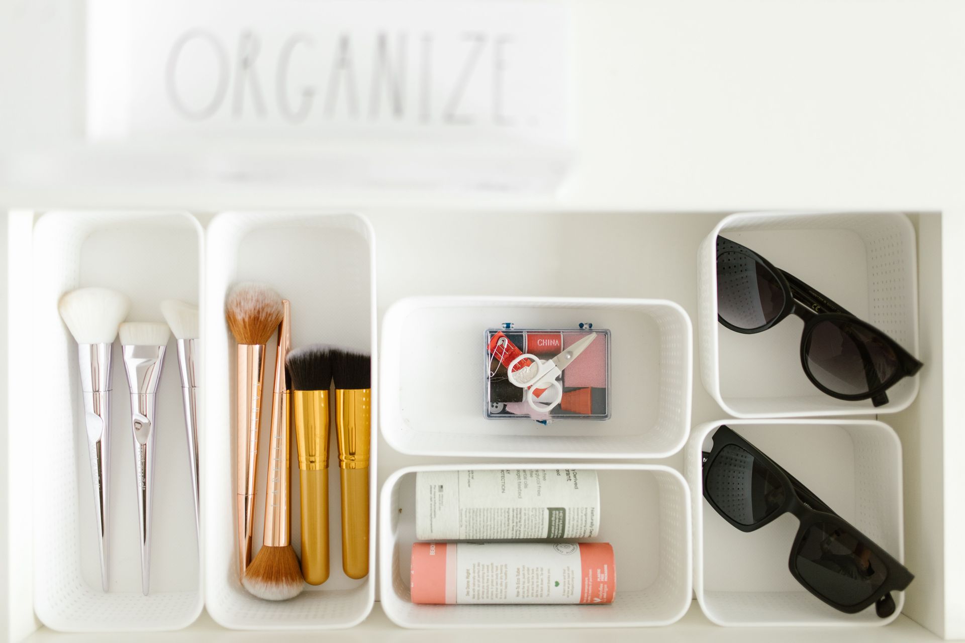 Organized makeup and skincare items in white drawer trays, including brushes, cosmetics, and sunglasses.