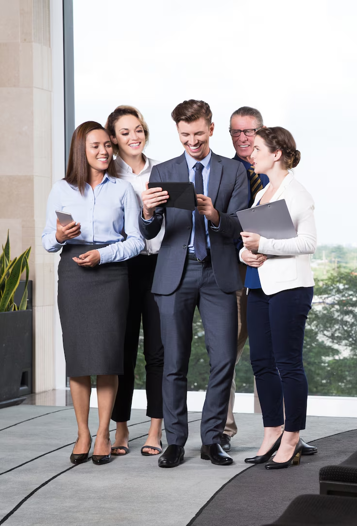 A group of business people are standing in front of a window looking at a tablet.