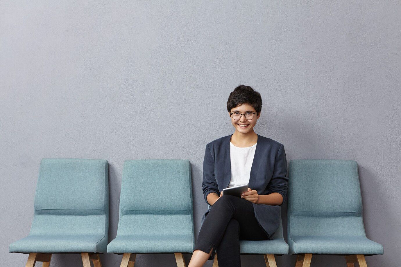 A woman is sitting in a row of chairs holding a tablet.