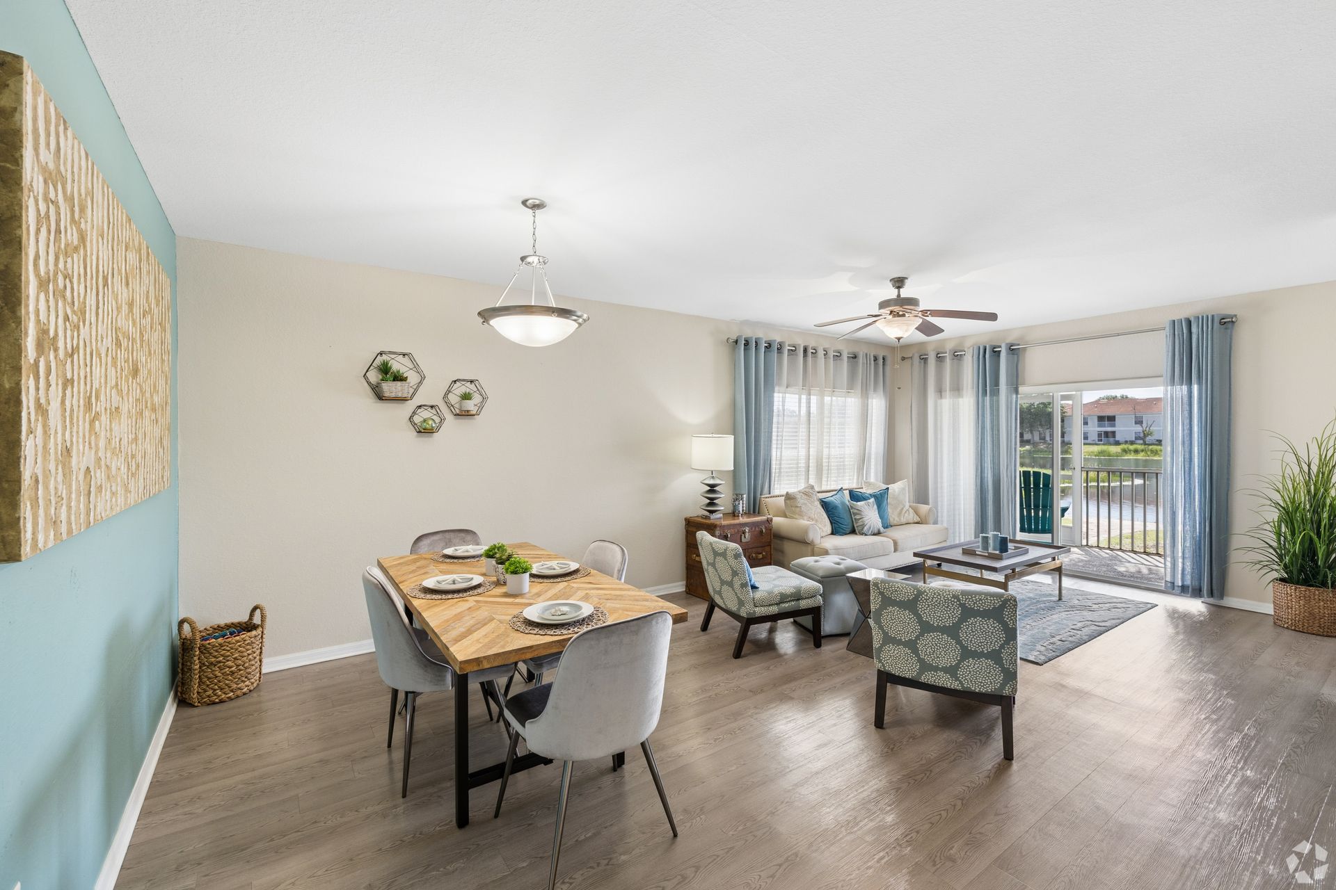 Bright dining and living room with table, sofas, large windows, and sliding glass doors to a balcony