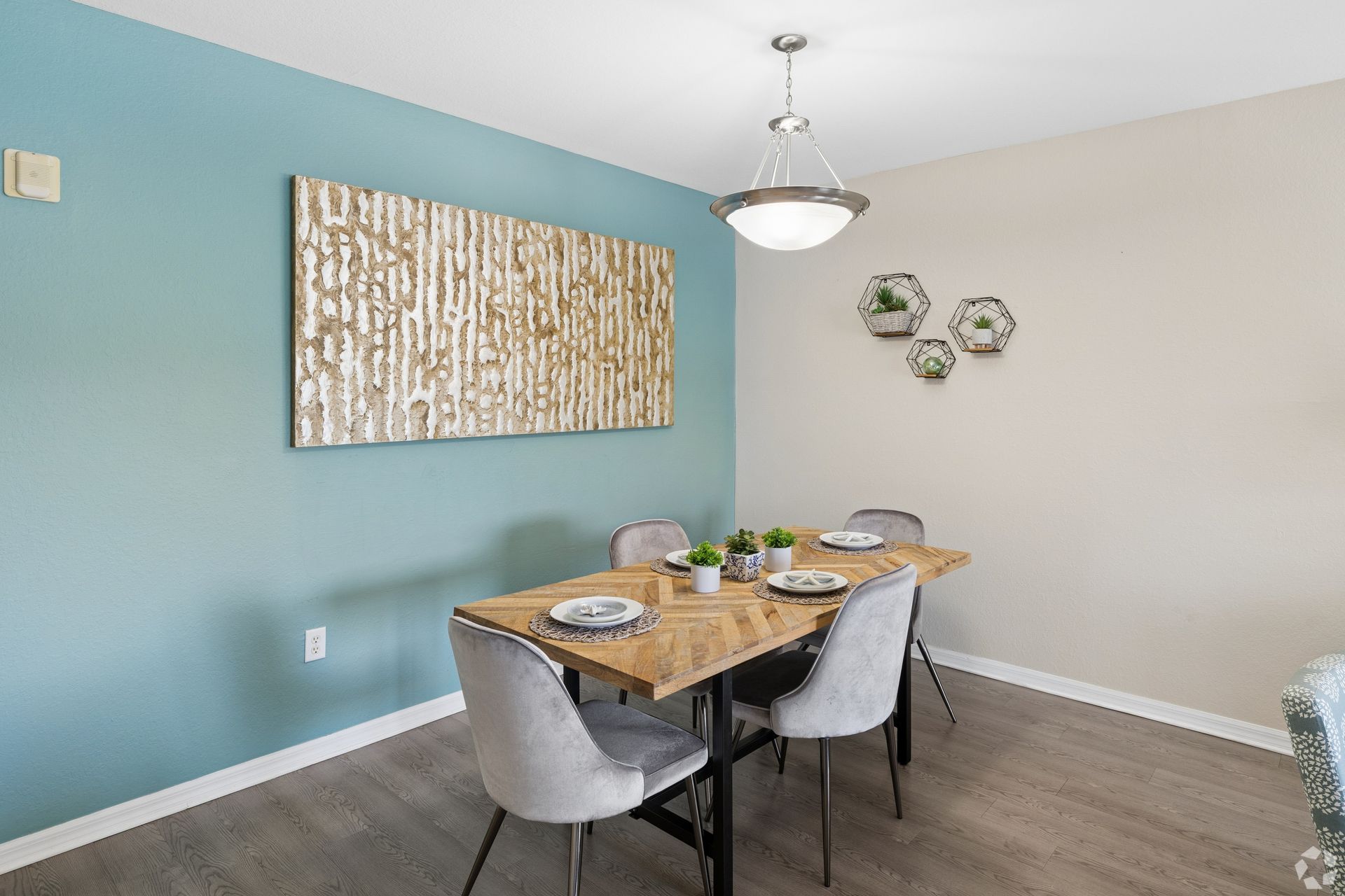 Modern dining room with blue and beige walls, wooden table, gray chairs, and wall decor