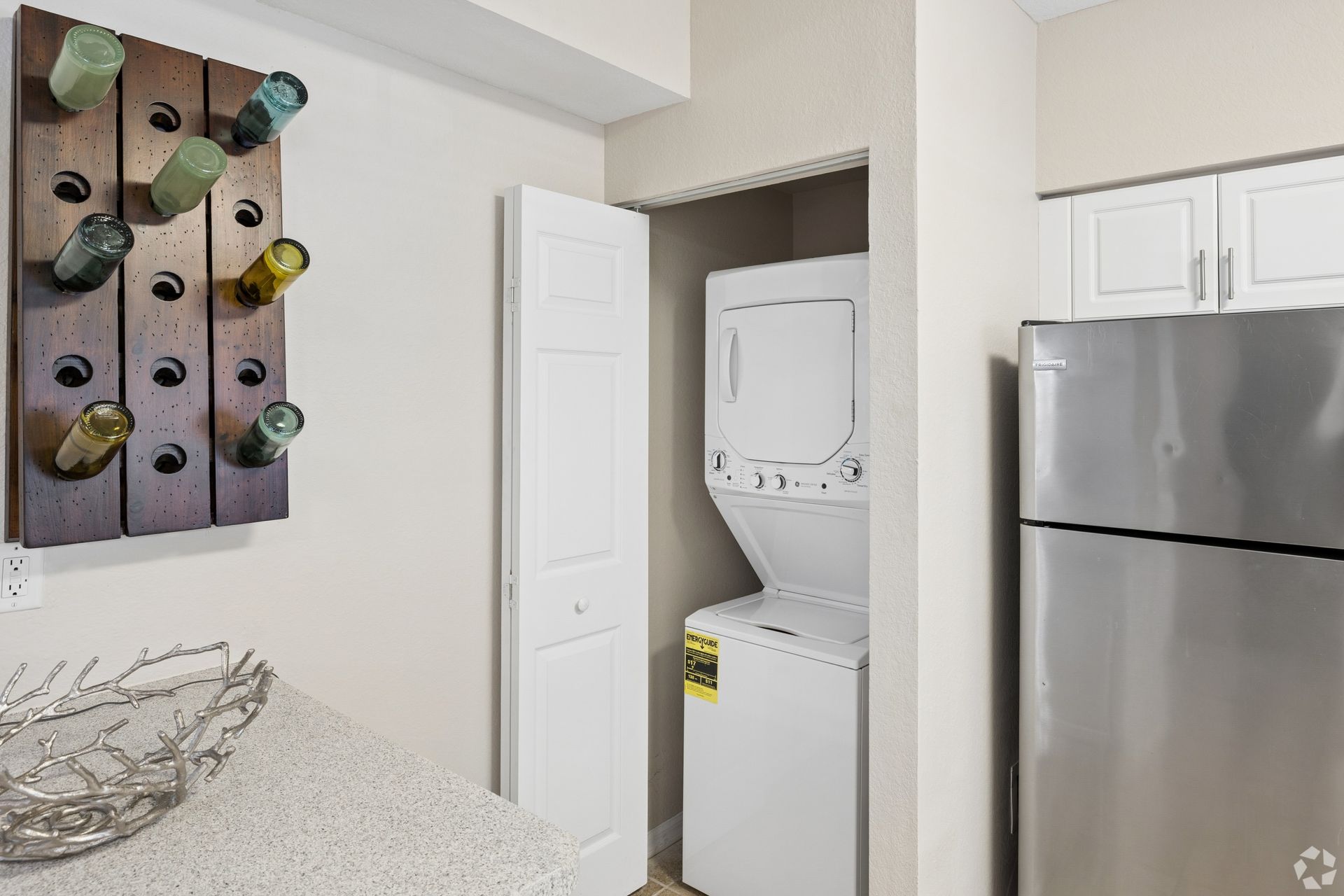 Compact laundry nook with stacked washer-dryer beside a stainless fridge and wall-mounted wine rack