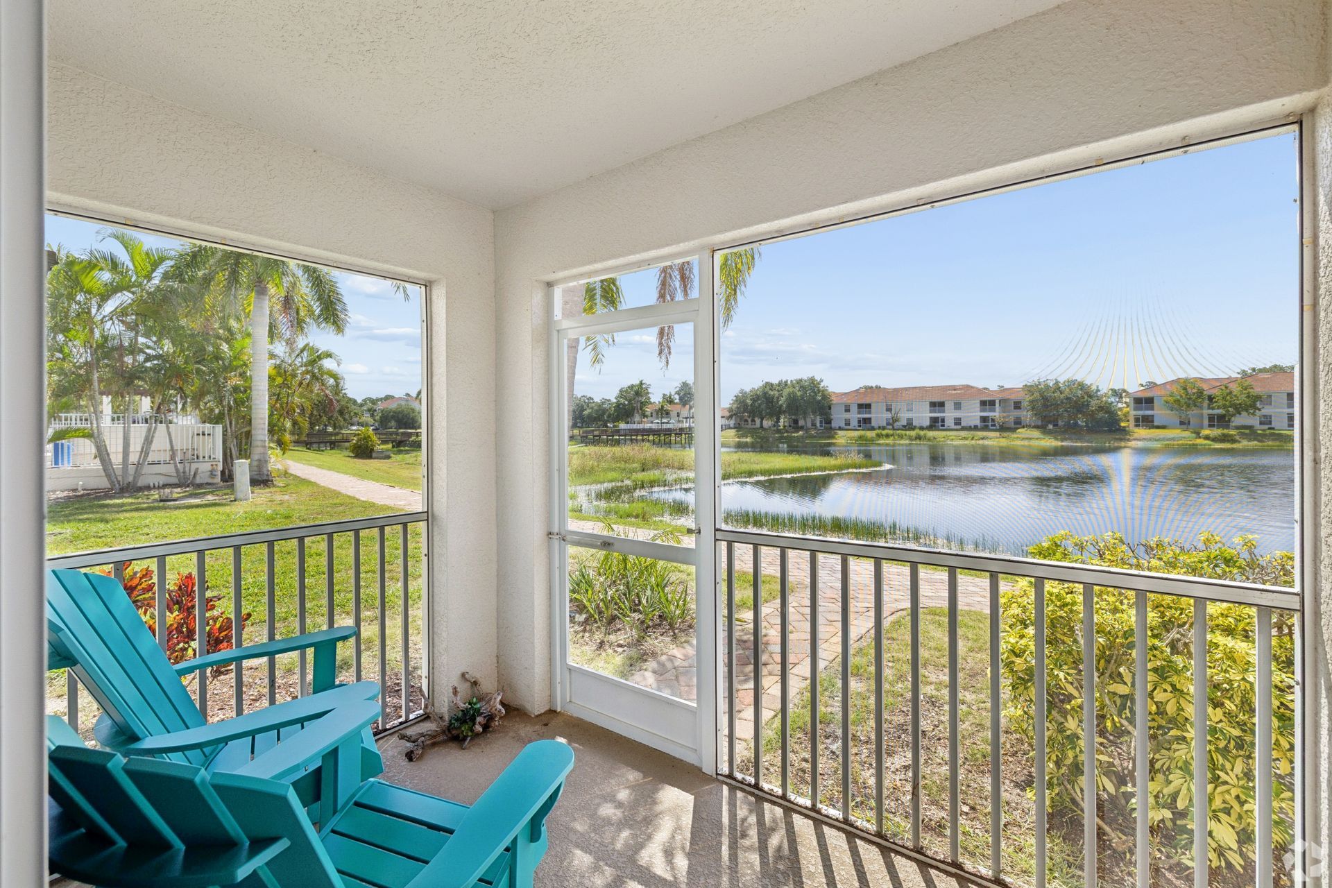 Covered balcony with turquoise chairs overlooking a lake and distant buildings