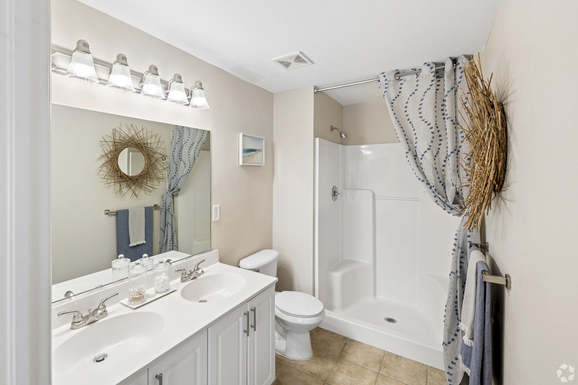 Bright bathroom with white vanity, mirror lights, toilet, and shower curtain with wreath decor