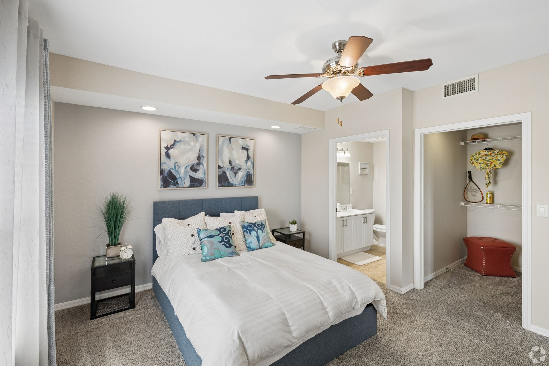 Spacious bedroom with a bed, ceiling fan, nightstand, and an open doorway to a bathroom.