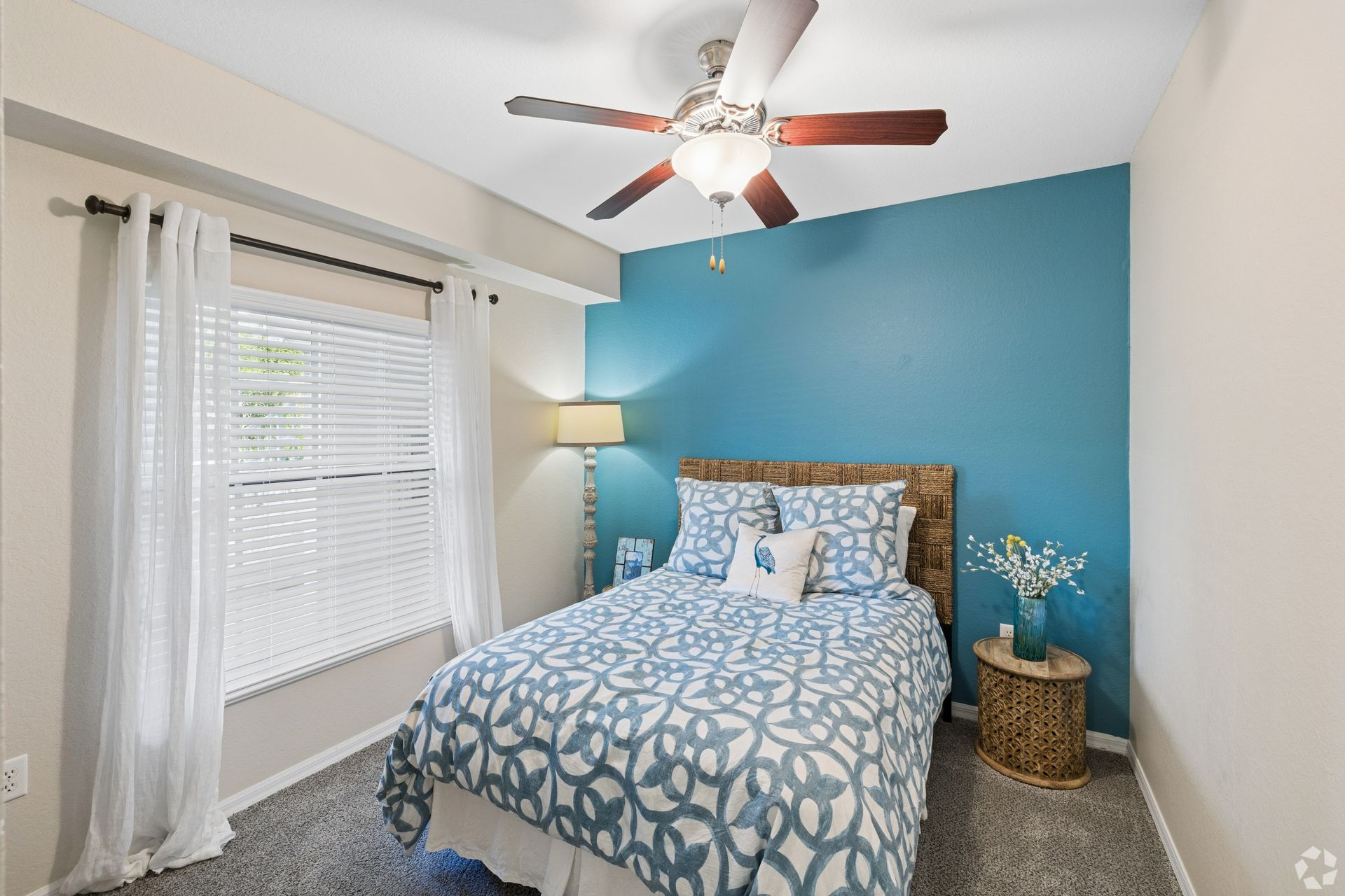 Bedroom with blue accent wall, white bed, ceiling fan, and window with sheer curtains.
