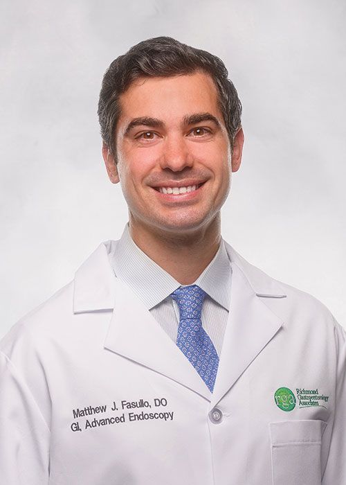 Portrait of a smiling doctor in a white coat and tie against a light gray background