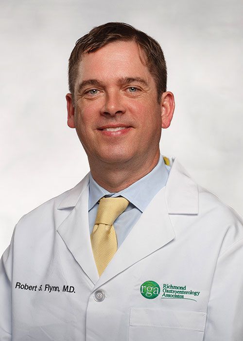 Portrait of a smiling doctor in a white coat and tie against a light gray background