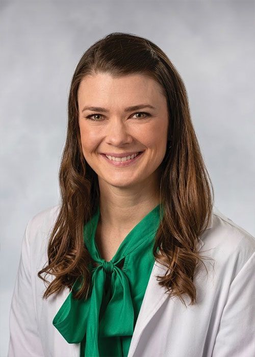 Portrait of a smiling doctor in a white coat and tie against a light gray background