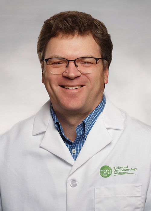 Portrait of a smiling doctor in a white coat and tie against a light gray background