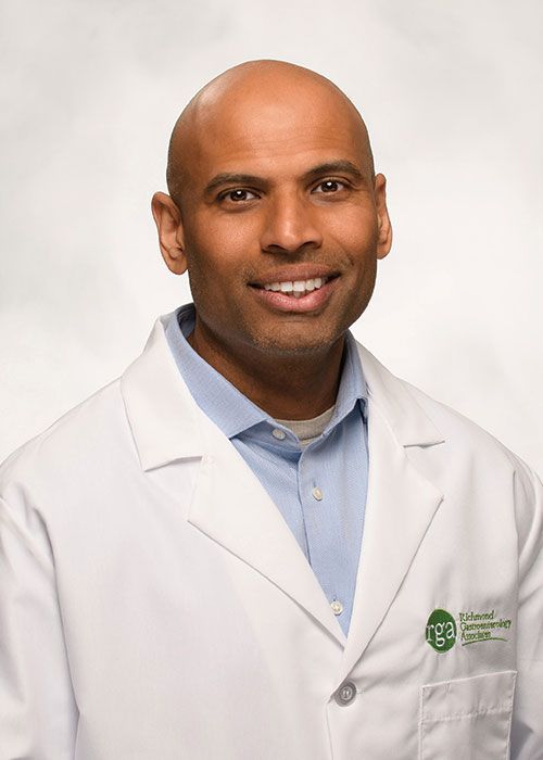Portrait of a smiling doctor in a white coat and tie against a light gray background
