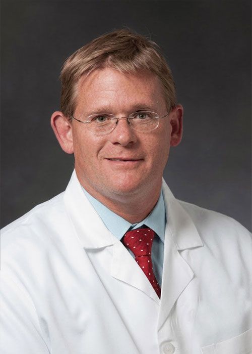 Portrait of a smiling doctor in a white coat and tie against a light gray background
