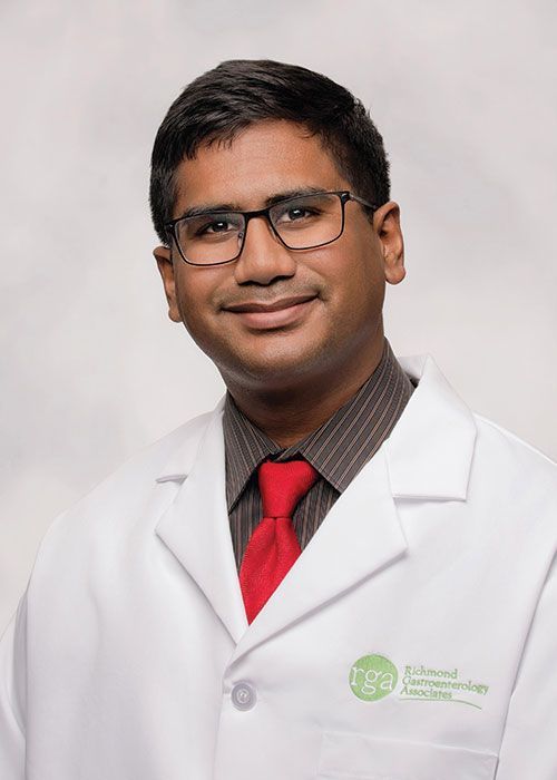 Portrait of a smiling doctor in a white coat and tie against a light gray background
