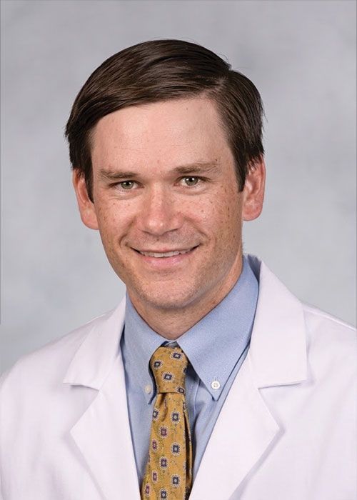 Portrait of a smiling doctor in a white coat and tie against a light gray background