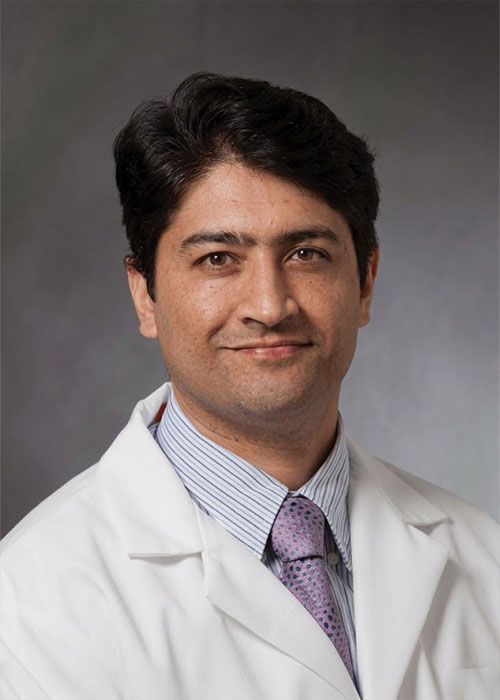 Portrait of a smiling doctor in a white coat and tie against a light gray background