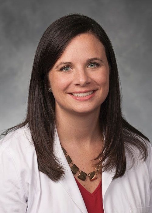 Portrait of a smiling doctor in a white coat and tie against a light gray background