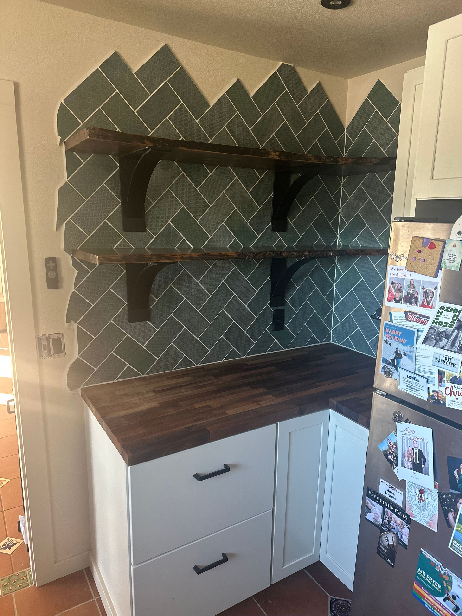 Kitchen corner with white cabinets, dark wood countertop and shelves, green tile backsplash.