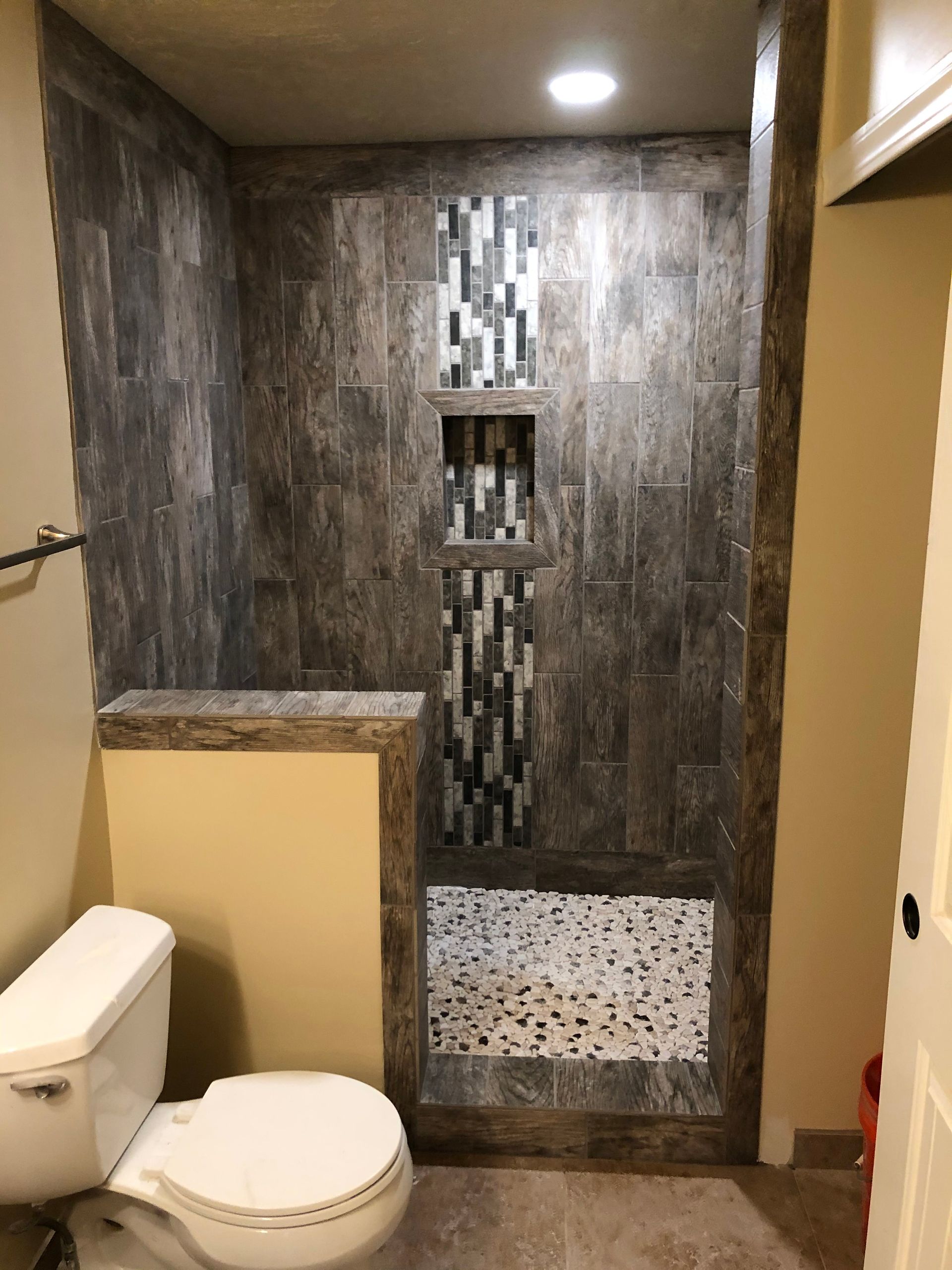 Bathroom with a walk-in shower. The shower has dark wood-look tile, inset shelves, and pebble-tiled floor.