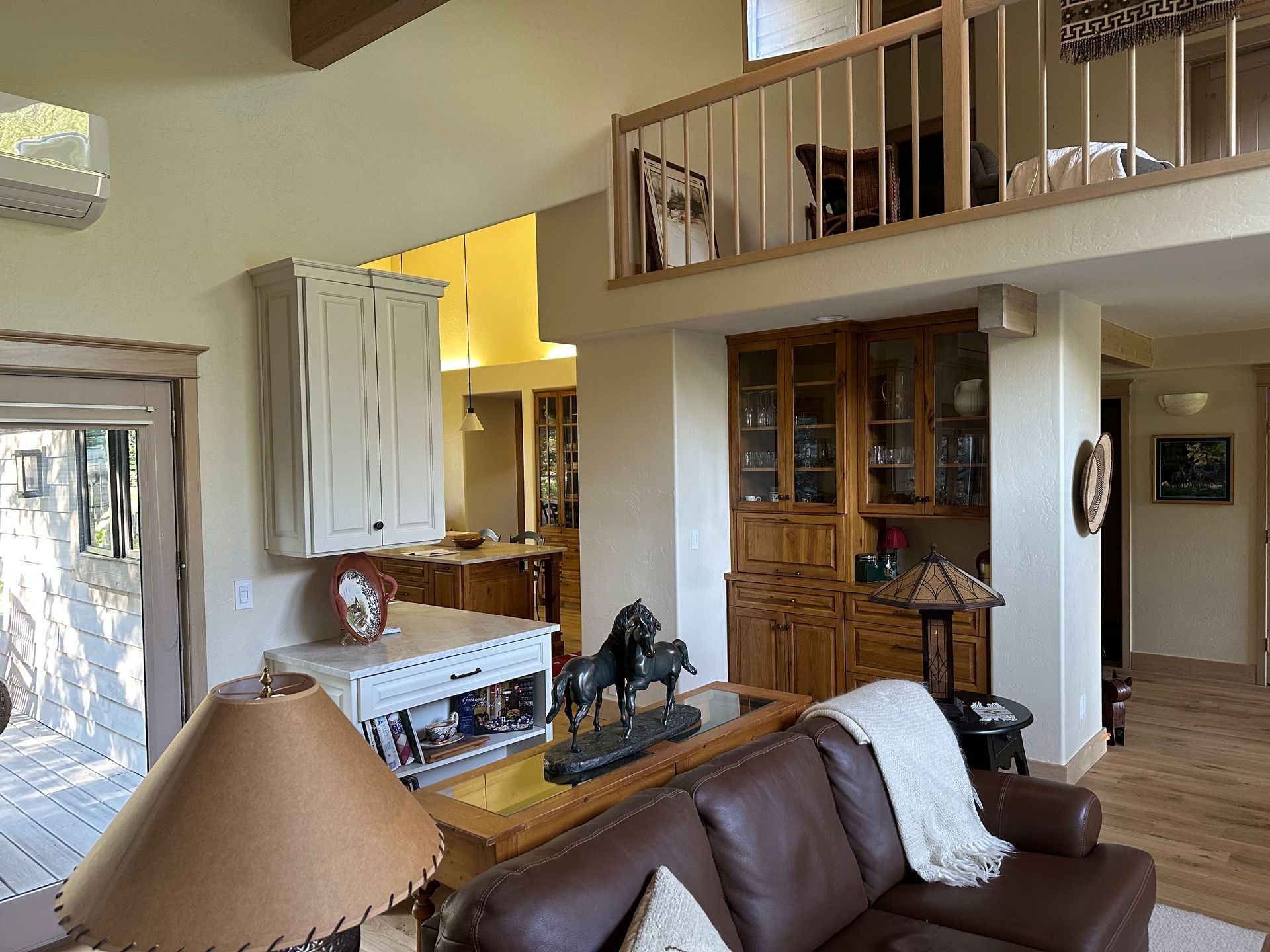 Living room with loft, brown leather sofa, wooden cabinets, and a horse statue on the table.