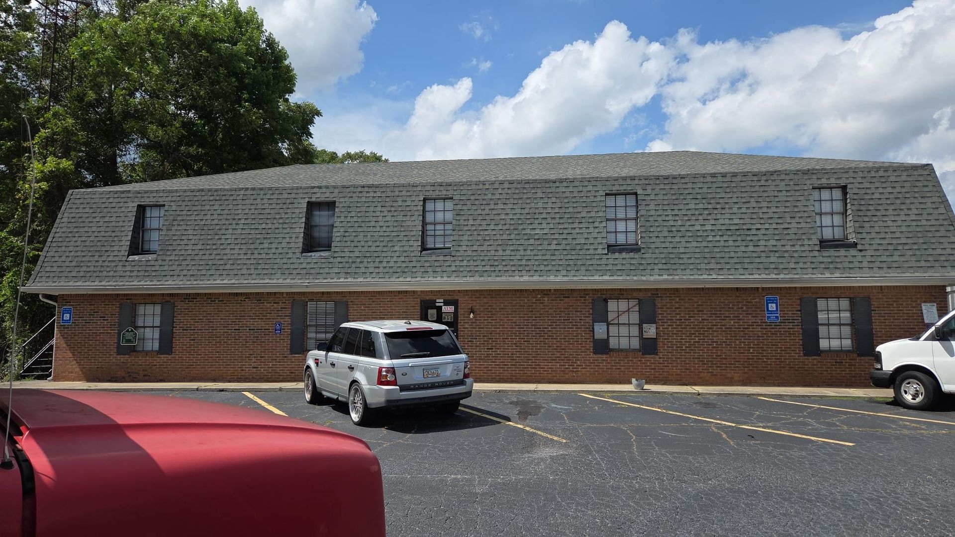 Two-story brick building with dark gray roof and several windows. A car is parked in front.