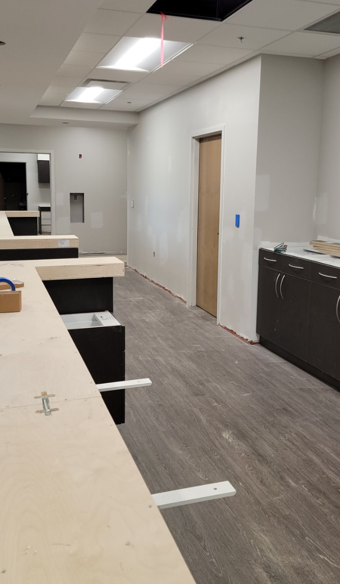 Interior view of a room under construction with white walls, wood flooring, and exposed ceiling.