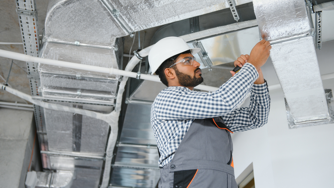 Construction worker in a hard hat working on ductwork in a building.