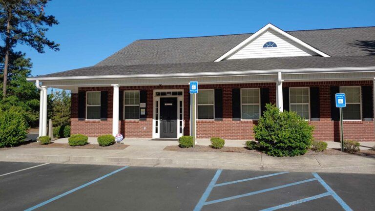 Exterior view of a brick building with a covered porch, blue parking signs, and a dark door.