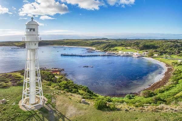White lighthouse overlooking a blue bay and green coastline under a partly cloudy sky