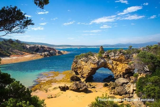 Coastal bay with turquoise water, sandy beach, and a rocky arch under a bright blue sky