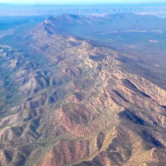 Aerial view of a long rocky mountain ridge with desert terrain and blue horizon.