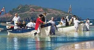 People launching small boats at a beach, with mountains and blue sky in the background