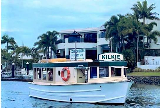 Small white tour boat on blue water near palm trees and a waterfront building, with “KIKLIE” sign.