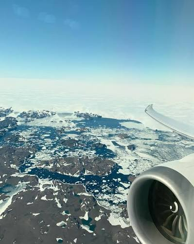 Airplane wing and engine above snowy Arctic landscape under a clear blue sky