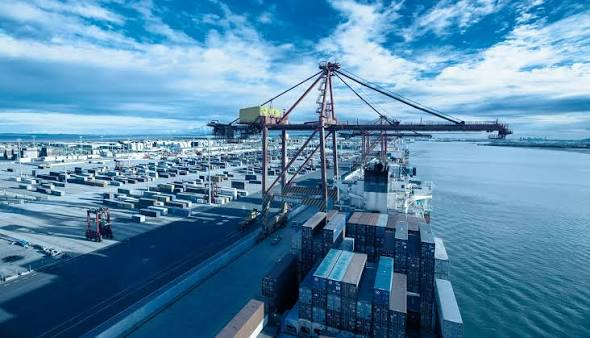Snowy container port with cranes and stacked shipping containers under a bright blue sky