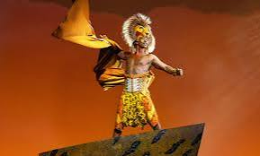 Costumed performer on a stage, waving a yellow flag against an orange background.