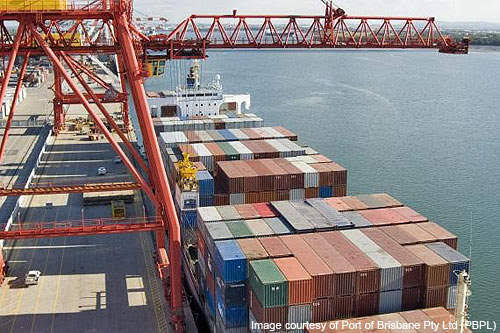 Shipping containers stacked on a cargo ship at a port with red cranes overhead