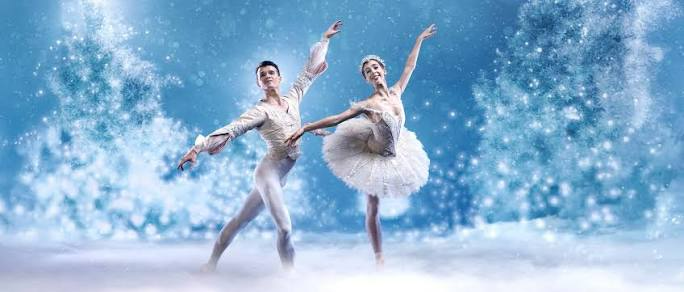 Two ballet dancers in white costumes posing against a blue snowy backdrop