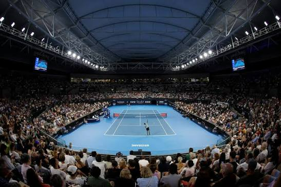 Packed indoor tennis arena with blue court and two players mid-match