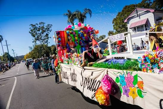 Colorful parade float decorated with flowers and balloons rolling down a sunny street