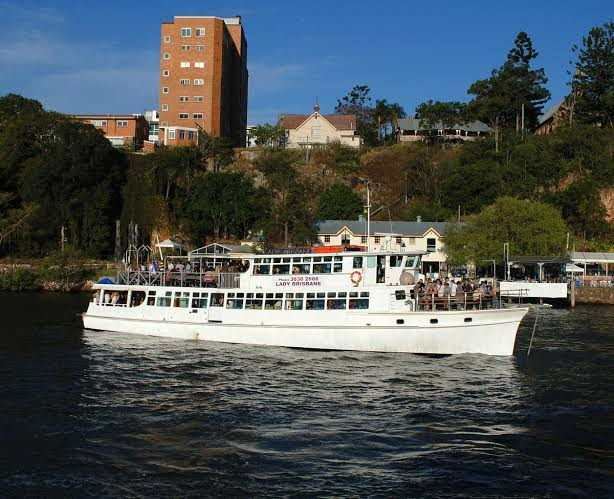 White ferry boat on a river with a hillside of buildings and trees in the background