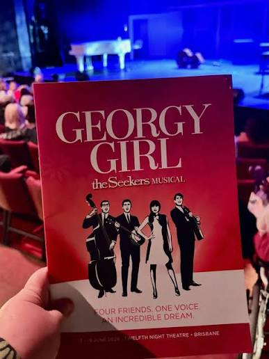 Hand holding a red Georgy Girl theater program in a blue-lit venue