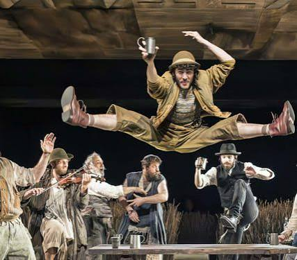 Five performers onstage, one leaping overhead, in cowboy-inspired costumes and hats
