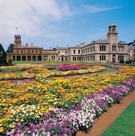Formal garden with colorful flower beds in front of a historic palace under a blue sky