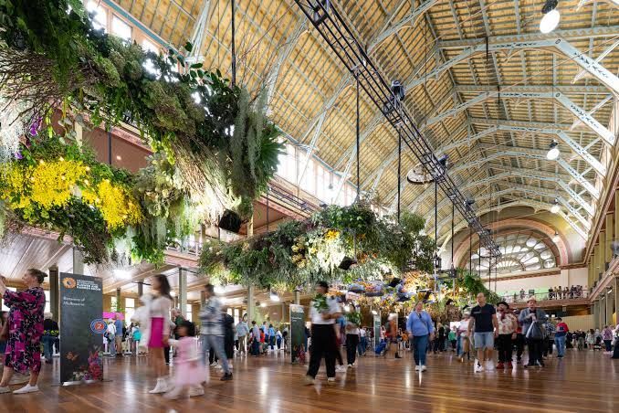 Flower-filled airport terminal with people walking under a high arched glass ceiling