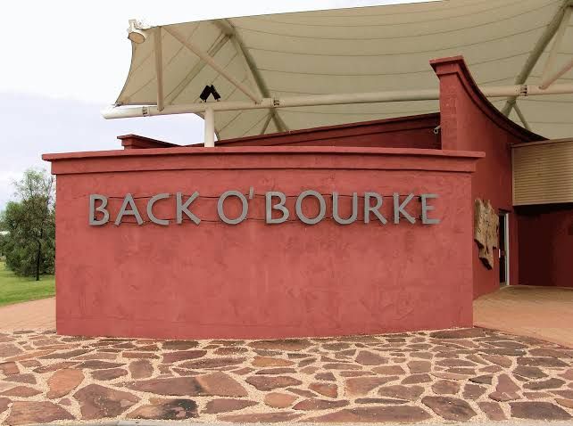 Entrance sign reading “Back O’ Bourke” on a red building with a tan roof and stone-paved foreground