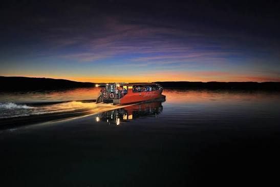Red rescue boat speeding across calm water at sunset, leaving a bright reflection and spray