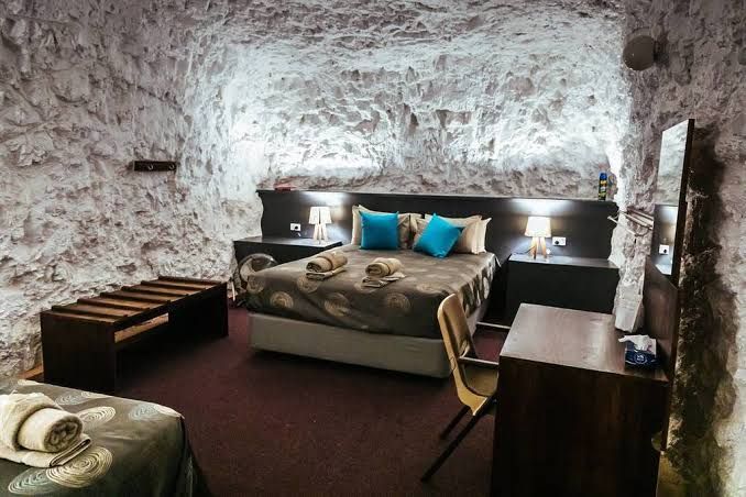 Stone-walled bedroom with a bed, teal pillows, warm bedside lights, and dark wood furniture.